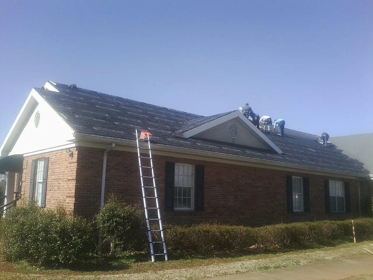 Crew tearing shingles off a brick ranch roof with a ladder set — Emergency Roof Repair work by our crew in Dillwyn