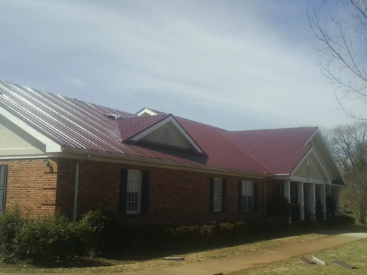 Red metal roof with gabled entries on a long brick building, from a Hail Damage Roof Repair job in Dillwyn