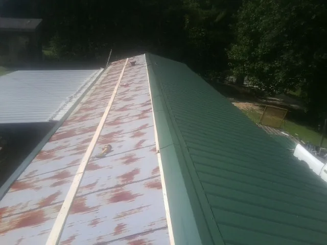 Old rusted panels beside newly installed green metal roofing — Wind Damage Roof Repair by Roofing Brothers in Dillwyn