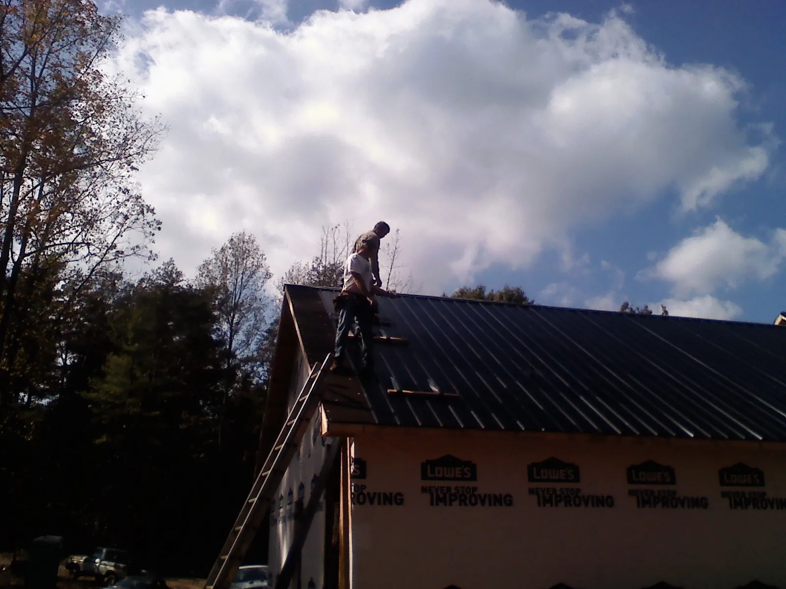 Roofer fastening dark metal panels high against a cloudy sky, from a Roof Inspection job in Dillwyn