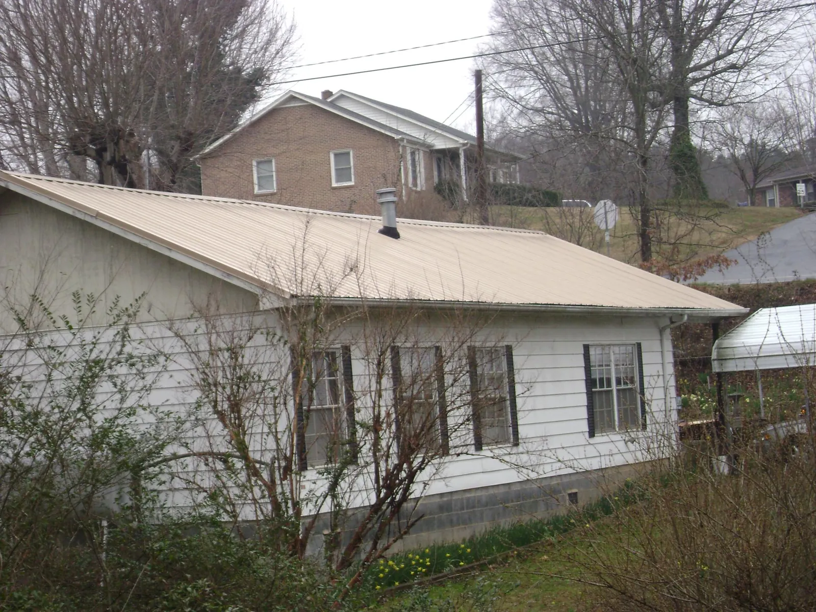 Tan metal roof on a white sided house set into a hillside — Commercial Roofing by Roofing Brothers in Dillwyn